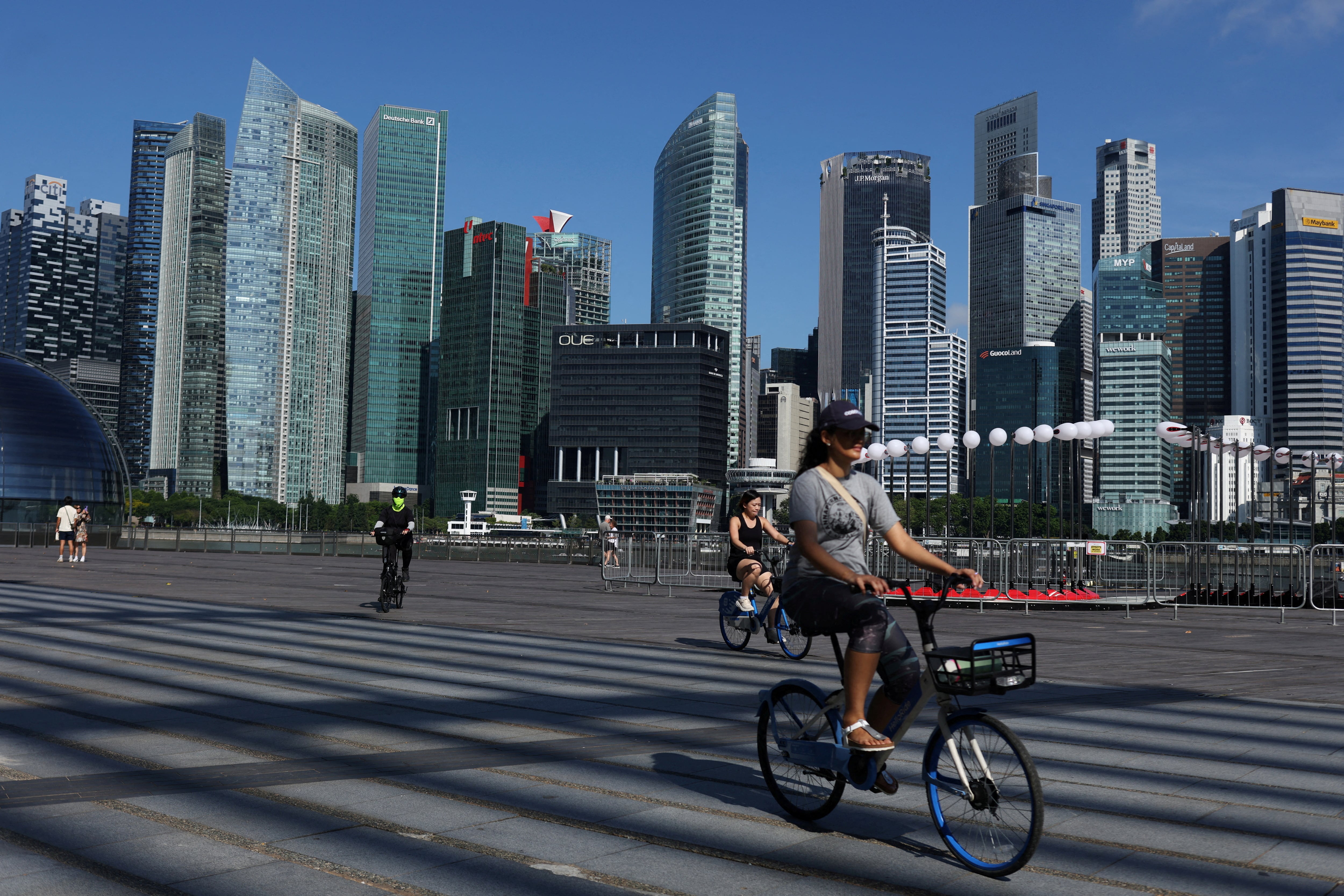 People ride bikes past the skyline of the central business district in Singapore